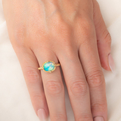 Gold ring featuring a vibrant Ethiopian opal stone, worn on a person's finger.