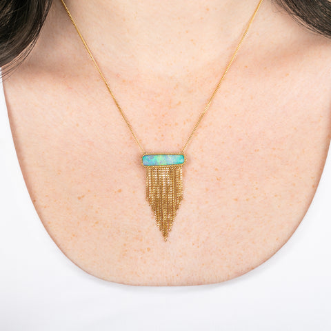 A necklace featuring an ethiopian opal draped with a gold tassel on a person