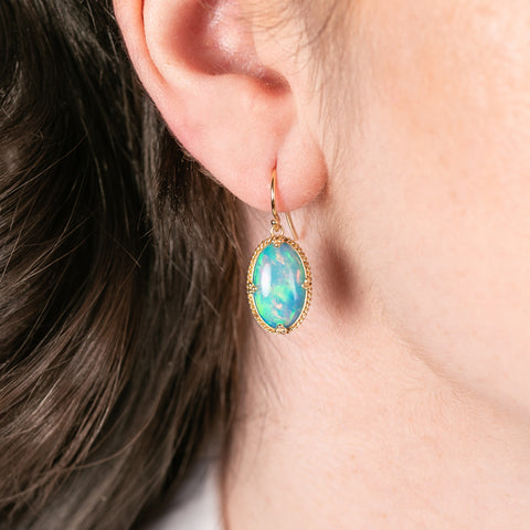 Gold earring with ethiopian opal stone worn by a person