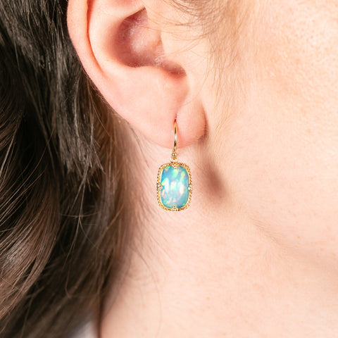 Gold earring with ethiopian opal gemstone worn by a person