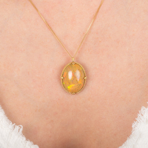 Gold necklace with an Ethiopian opal pendant on a person's neck