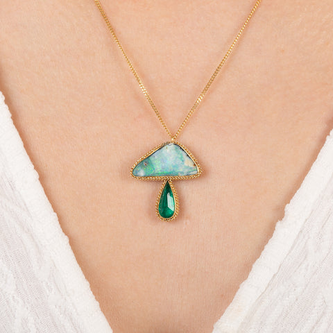 Gold necklace with a mushroom pendant featuring an emerald and opal stone on a person