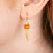 Gold earrings featuring fire opal gemstones and gold chain tassels, shown worn on a model's ear.