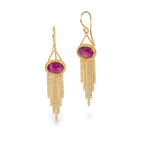 A pair of gold dangle earrings with oval pink fluorite gemstones and cascading chain tassels, shown against a white background.