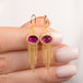 A pair of gold dangle earrings with oval pink fluorite gemstones and cascading chain tassels, held in hand.