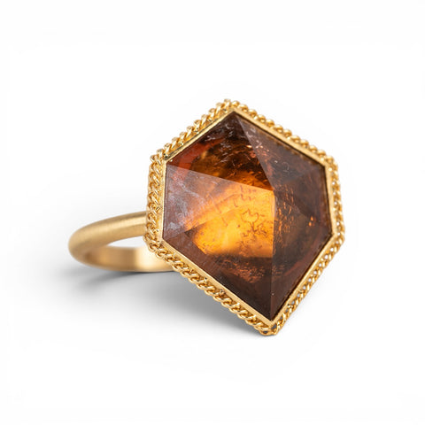 Hexagonal tourmaline gemstone ring with gold band on a white background