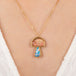 Gold pendant with a mushroom design combining a tourmaline stone with a boulder opal stone on a person