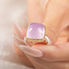 A square cushion-cut kunzite gemstone ring with a gold bezel and a sterling silver band, held in hand.