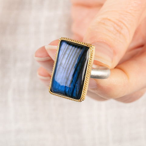 Close up of a person holding a handmade fine jewelry labradorite ring set in 18k gold with a sterling silver band