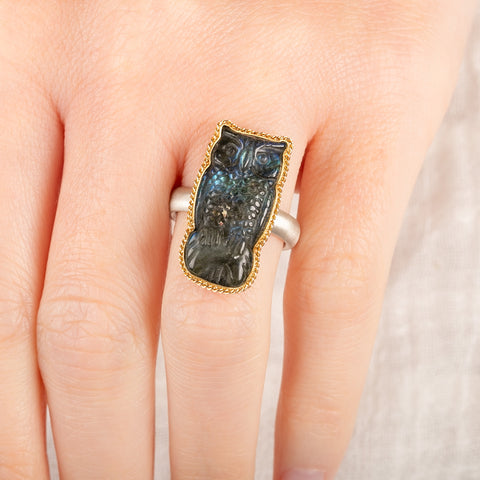 Close up of a person wearing a handmade fine jewelry labradorite owl ring set in 18k gold with a sterling silver band