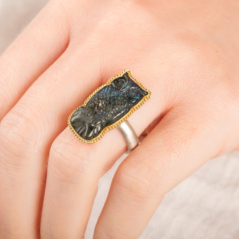 Close up of a person wearing a handmade fine jewelry labradorite owl ring set in 18k gold with a sterling silver band