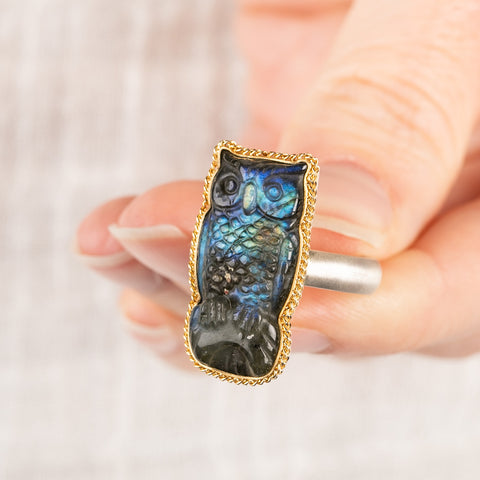 Close up of a person holding a handmade fine jewelry labradorite owl ring set in 18k gold with a sterling silver band