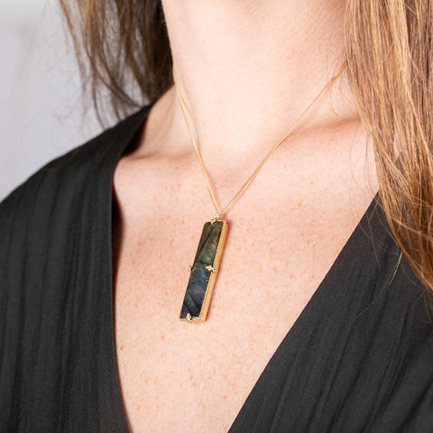 Handcrafted gold necklace with a labradorite gemstone pendant worn by a person against a neutral background.