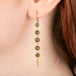 A gold earrings featuring a row of five green diamonds shown worn in a person's ear.