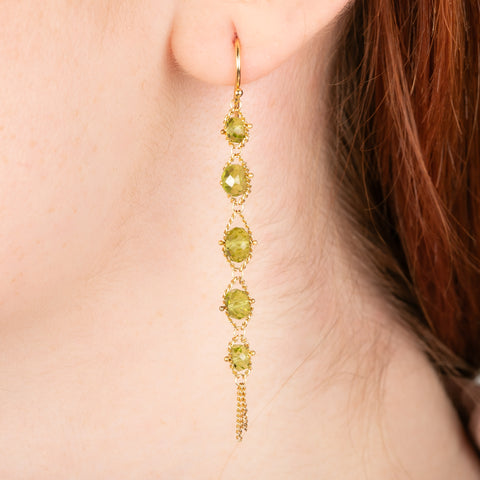 A gold earrings featuring a row of peridot gemstones, shown worn in a person's ear.