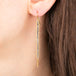 Gold earring featuring row of grey diamonds, worn on a person's ear.