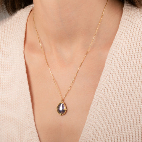 Gold necklace featuring a mabe pearl set in a handcrafted 18k gold bezel, worn on a person's neck.
