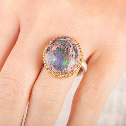 Close up of a person wearing a ring with a mexican opal stone and 18k gold bezel with a sterling silver band