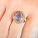 Close up of a person wearing a ring with a mexican opal stone and 18k gold bezel with a sterling silver band