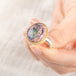 Close up of a person holding a ring with a mexican opal stone and 18k gold bezel with a sterling silver band