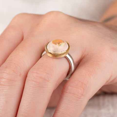 Close-up of a hand wearing a ring with a mexican opal gemstone set in an 18k gold bezel with a sterling silver band