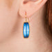 Gold earrings featuring large, blue moonstones, worn in a model's ear.