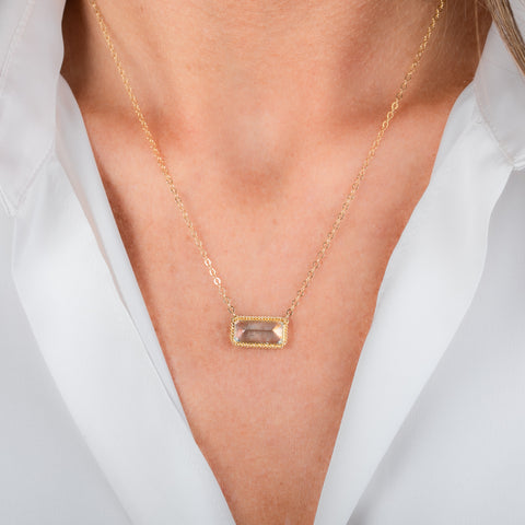 A gold necklace featuring a moonstone gem, worn on a person's neck.