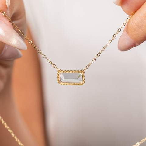 A close up of a gold necklace featuring a moonstone gem held in hand