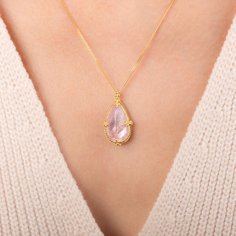 Teardrop-shaped morganite necklace set in an 18k gold bezel and matching chain, worn on a person's neck.
