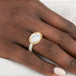 Close-up of a hand wearing a gold and silver ring with a white mother of pearl stone on a white background