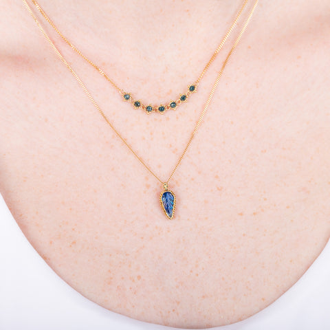 A model wears an 18k gold and blue diamond chain necklace paired with a small carved leaf moonstone necklace.