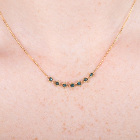 A close up of a model wearing an 18k gold and blue diamond chain necklace.