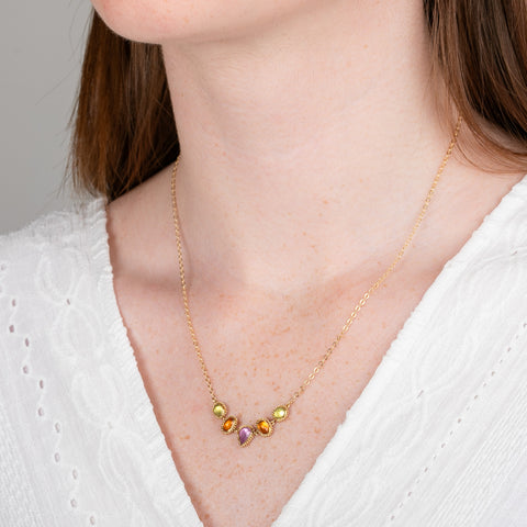 A gold necklace featuring a row of sapphire gemstones in different shapes and colors, shown worn on a model's neck.
