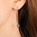A close-up of a gold dangle earring with a Nigerian sapphire gemstone, shown worn on a person's ear.