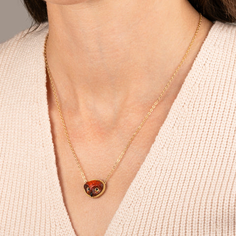 Gold necklace featuring a carved owl pendant made from garnet with an onyx beak, worn on a person's neck.