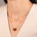 Gold necklace featuring a carved owl pendant made from garnet with an onyx beak, worn on a person's neck.