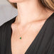 Gold necklace with a petite emerald gemstone set in a handmade gold bezel worn on a person.
