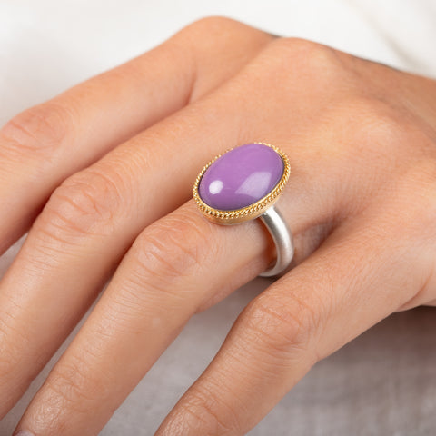 A gold and silver ring with a purple phosphosiderite stone, worn on a person's hand.