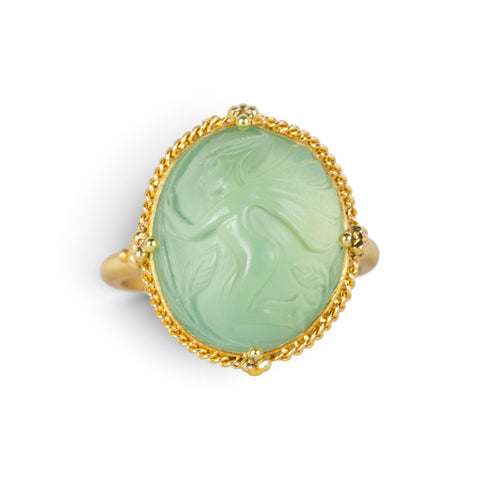 A gold ring featuring a prehnite with a fairy design carved in it, shown against a white background.