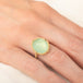 A gold ring featuring a prehnite with a fairy design carved in it, worn on a person's finger.