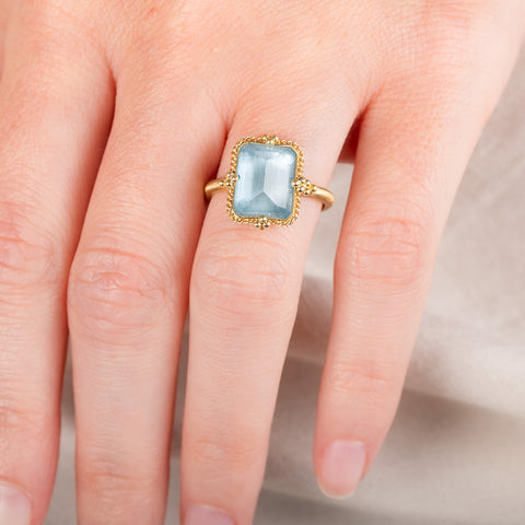 A model wears a handmade 18k yellow gold ring featuring a rectangular aquamarine gemstone.