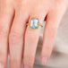 A model wears a handmade 18k yellow gold ring featuring a rectangular aquamarine gemstone.