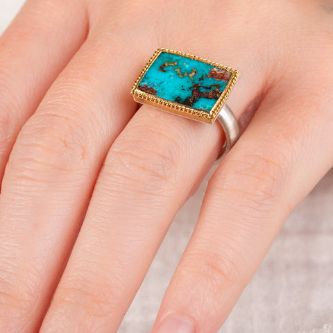 Close up of a hand wearing a turquoise ring with gold bezel and silver band