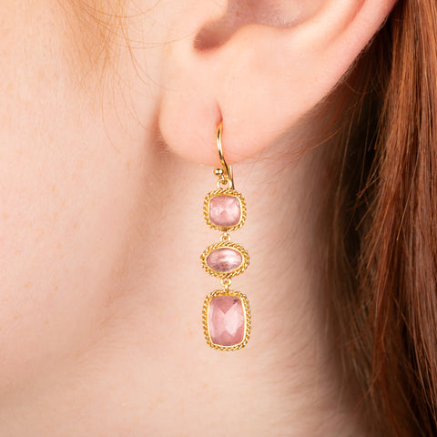 Gold earrings featuring a trio of rhodochrosite gemstones in varying shapes, shown worn in a person's ear.