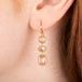 Gold earrings featuring a trio of rhodochrosite gemstones in varying shapes, shown worn in a person's ear.