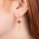 Gold earrings featuring rhodolite garnet gemstones and gold chain tassels, shown worn in a person's ear.