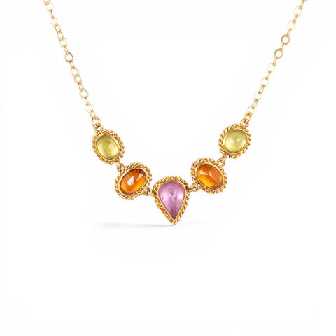 A gold necklace featuring a row of sapphire gemstones in different shapes and colors, shown against a white background.