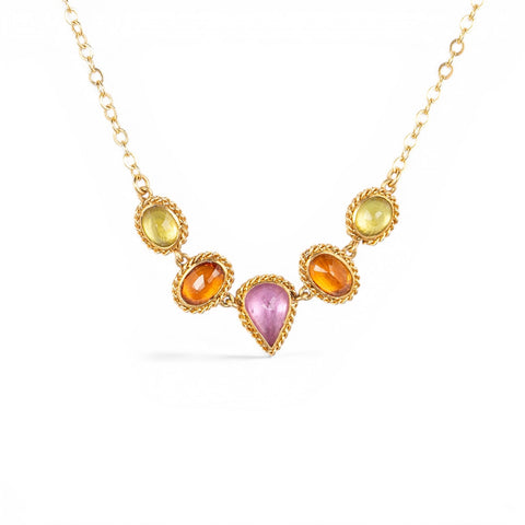 A gold necklace featuring a row of sapphire gemstones in different shapes and colors, shown against a white background.