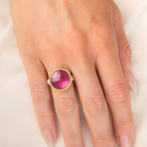Gold and silver ring featuring a bright pink sapphire gemstone, worn on a person's finger.