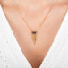 Gold necklace with a a spessartite gemstone adorned with a gold tassel on a person wearing a white top.